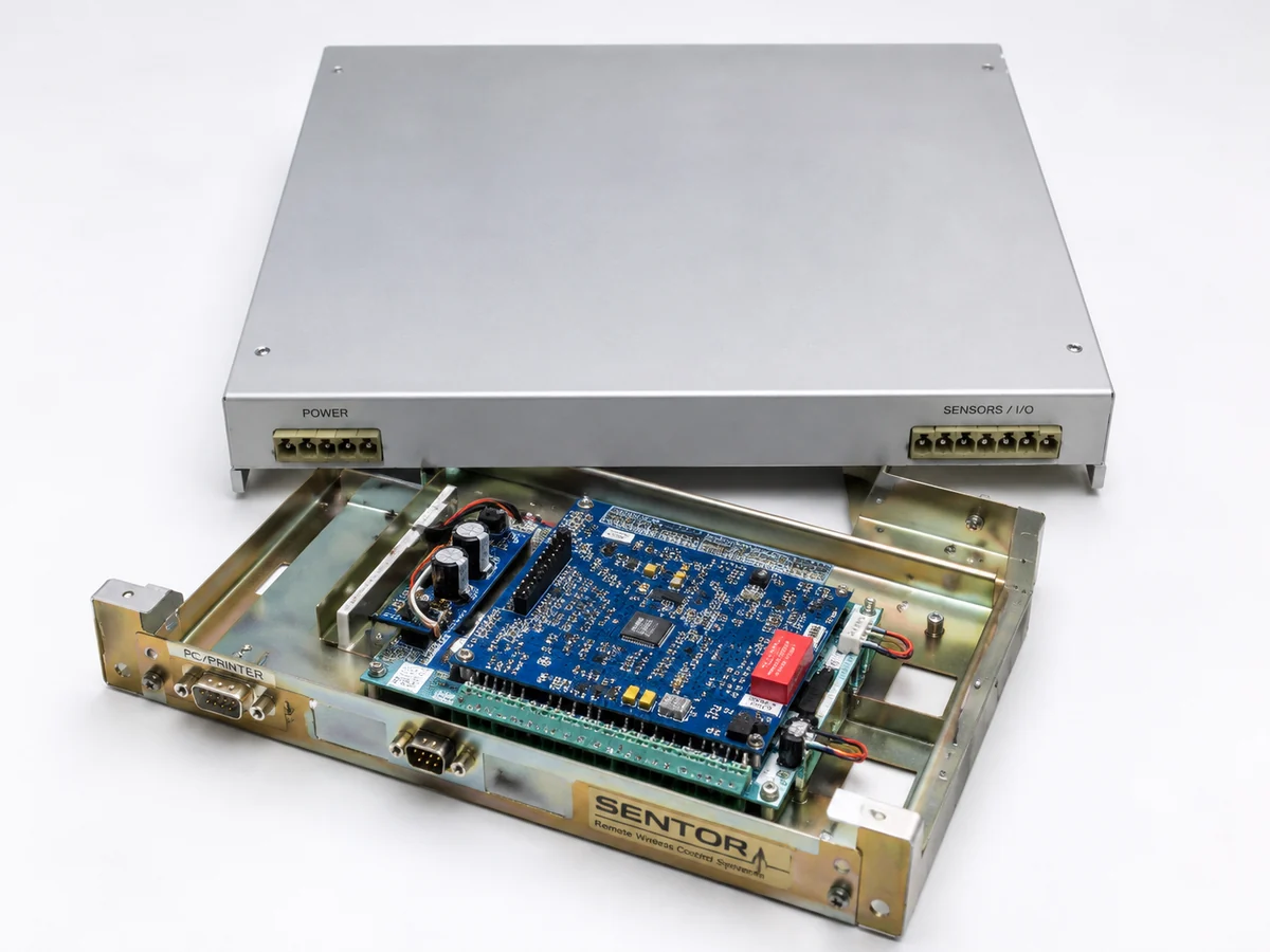 Sentor ST3000S reinforced security housing shown with the lid lifted clear, exposing the controller board, power and sensor I/O terminal blocks and serial connectors